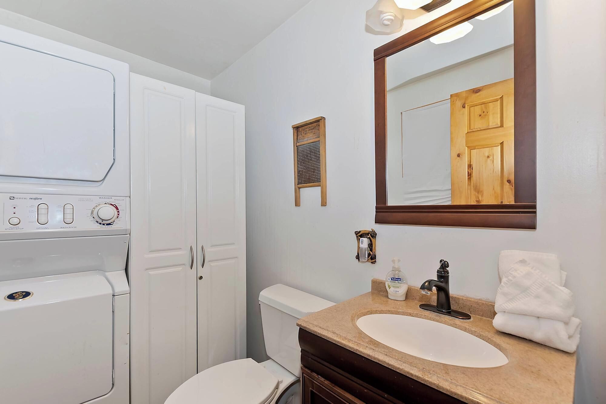Een badkamer met een wit toilet, een wastafel met een spiegel erboven en een wasmachine.