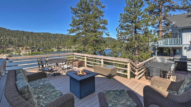 A deck with outdoor furniture, a fire pit, and a view of a lake surrounded by trees. - Walking Distance to Boulder Bay! Lakeviews! PET FRIENDLY! Internet! Darts & Poker Table! (Big Bear Lake)