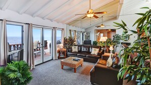 A spacious living area with a large sofa, a coffee table, and a television. There are multiple windows offering a view of the ocean. - 2B | 2B Villa, OCEAN VIEWS, NO STEPS, Golf Cart, 2 private balconies, electric f (Avalon)