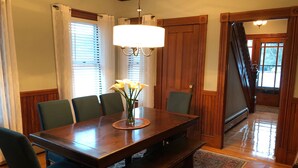 Ein Esszimmer mit Holztisch, grünen Stühlen, einer Blumenvase und einem Kronleuchter.
