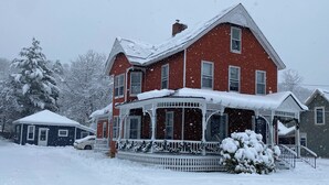 Ein großes rotes Haus mit Veranda und überdachter Eingangspforte, umgeben von Schnee.