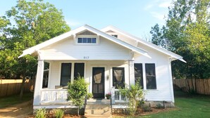 A white single-story house with a front porch, a small tree in front, and a number '917' on the front. - The Bell House | Modernized Bungalow Near Main Street & Hwy 290 Wineries (Fredericksburg)