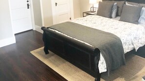 A bedroom with a bed, a bench, a nightstand, and a door. - The Bell House | Modernized Bungalow Near Main Street & Hwy 290 Wineries (Fredericksburg)