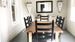 A dining room with a wooden table and chairs, a hanging light fixture, and a wall-mounted mirror. - The Bell House | Modernized Bungalow Near Main Street & Hwy 290 Wineries (Fredericksburg)