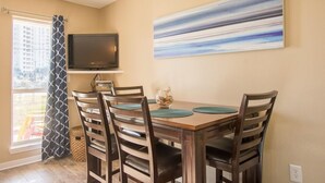 A dining area with a wooden table, four chairs, a flat-screen TV, and a large abstract painting on the wall.