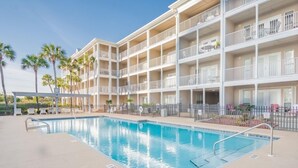 A hotel with a pool, multiple balconies, and palm trees.