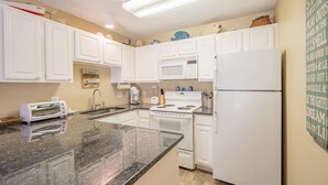A kitchen with white cabinets, a granite countertop, a stove, a refrigerator, and a microwave.