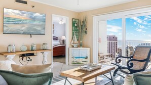 A living room with a large TV, a wooden coffee table, and a view of the balcony. - The Islander 715 | Stunning Panoramic Gulf & Harbor Views | Newly Updated (Destin)