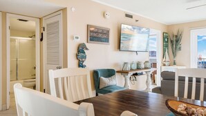 A dining area with a wooden table, white chairs, and a teal sofa. - The Islander 715 | Stunning Panoramic Gulf & Harbor Views | Newly Updated (Destin)