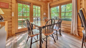 A wooden dining room with a chandelier, large windows, and a view of the outdoors. - ER43 Tulip Tree – 3BR Cabin w/ Hot Tub, Arcade, Pool, & Prime Pigeon Forge Spot (Pigeon Forge)