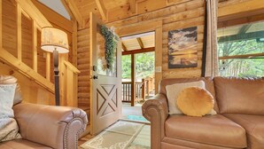 A wooden interior with a leather sofa, a staircase, and a door leading outside. - ER43 Tulip Tree – 3BR Cabin w/ Hot Tub, Arcade, Pool, & Prime Pigeon Forge Spot (Pigeon Forge)