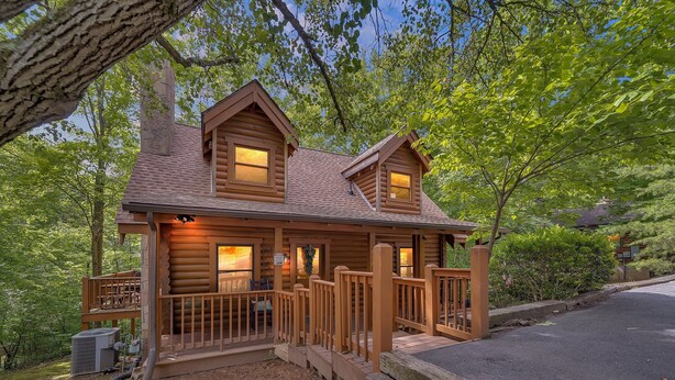 A log cabin with a porch, a covered deck, and a small front yard. - ER43 Tulip Tree – 3BR Cabin w/ Hot Tub, Arcade, Pool, & Prime Pigeon Forge Spot (Pigeon Forge)