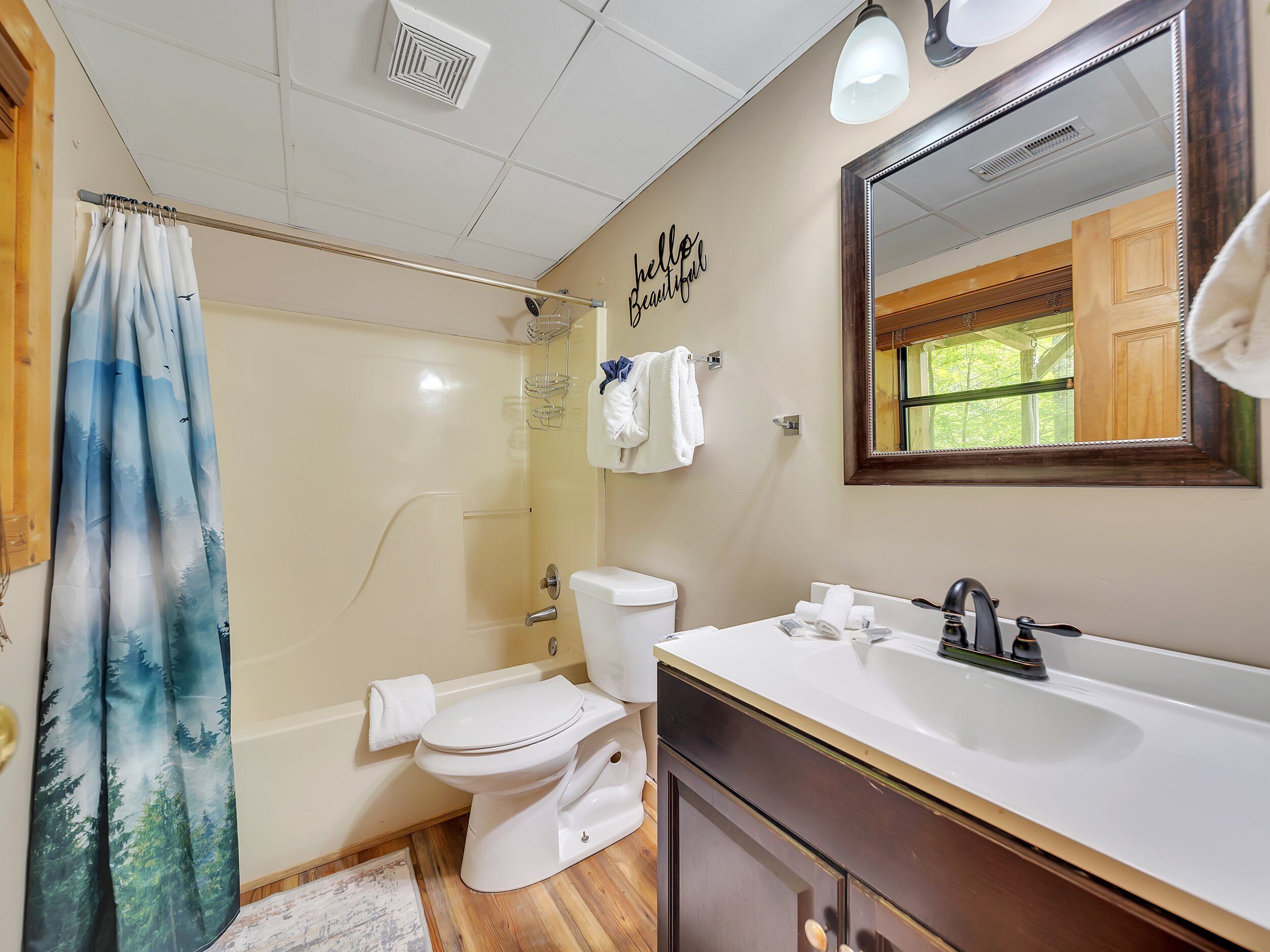 A bathroom with a shower curtain, toilet, sink, and a mirror.