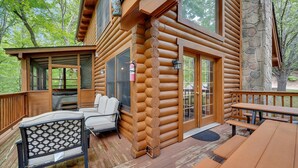 A log cabin with a deck, outdoor seating, and a stone wall. - ER43 Tulip Tree – 3BR Cabin w/ Hot Tub, Arcade, Pool, & Prime Pigeon Forge Spot (Pigeon Forge)