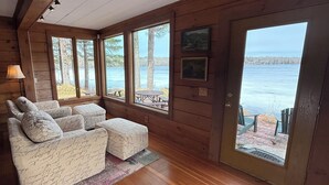 Eine Hütte mit Holzinnenausstattung, einem Sofa mit handgeschriebenen Notizen, einer Tür zu einer Terrasse und Blick auf einen See.