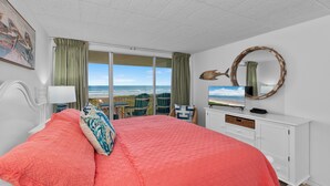 Un dormitorio con una cama grande, televisión, cómoda y vista al océano.