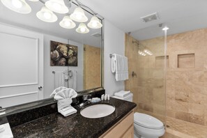 Une salle de bain moderne avec un comptoir en granit noir, un lavabo blanc, un grand miroir et une douche à parois de verre.