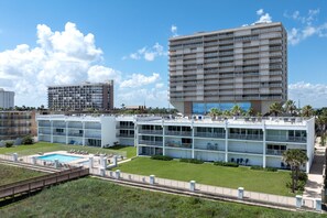 A modern hotel with multiple floors, a swimming pool, and a well-maintained lawn.