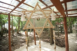 A geometric, woven structure hanging from a wooden framework in a forested area. - Magical jungle Eco Cabana in Tulum Mexico (Macario Gómez)