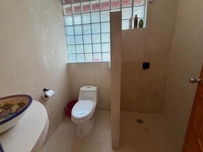 A bathroom with a toilet, a shower, a window with patterned glass, and a toilet paper holder. - Magical jungle Eco Cabana in Tulum Mexico (Macario Gómez)