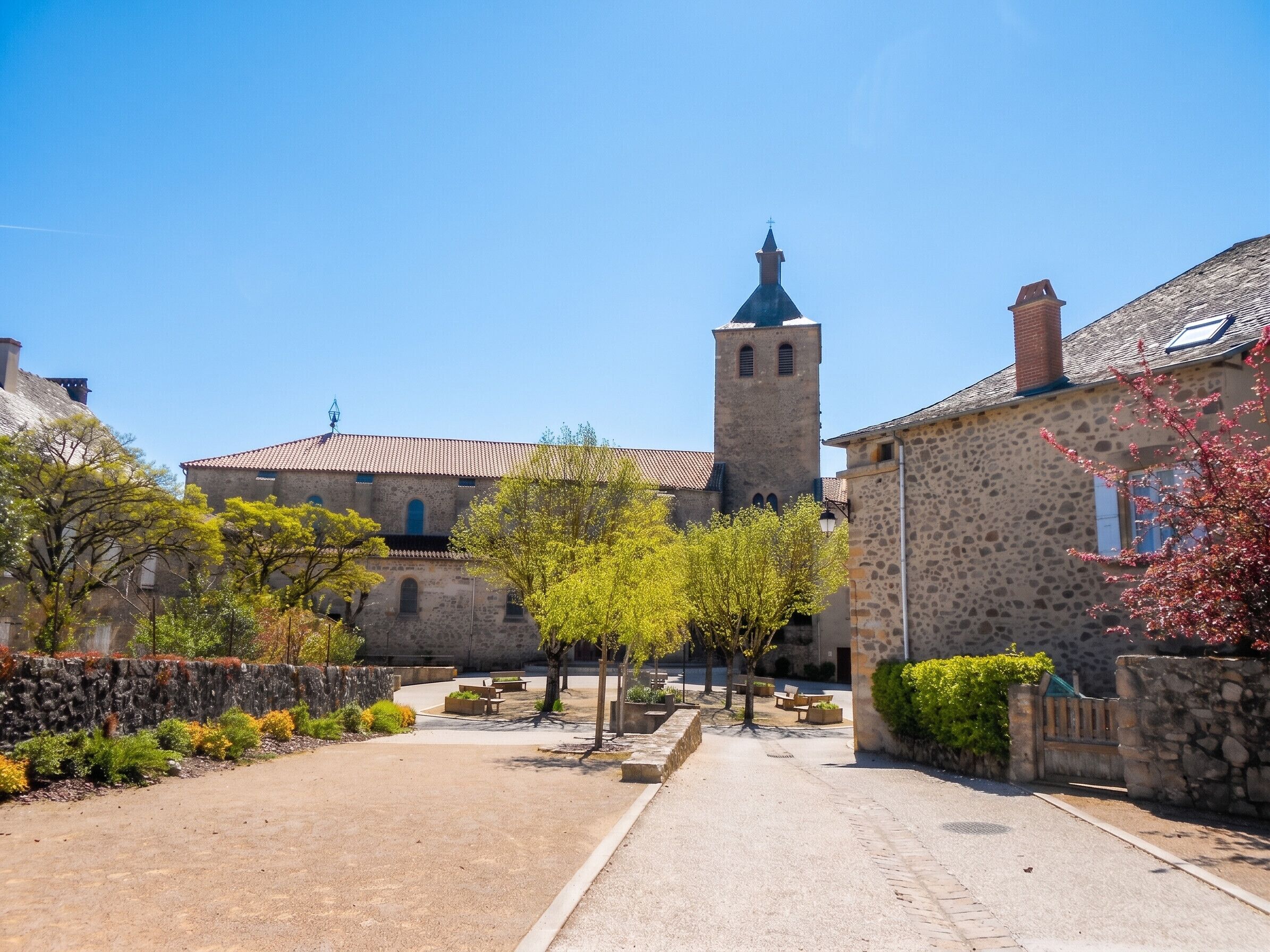 Un edificio histórico de piedra con una torre, un patio empedrado y bancos.
