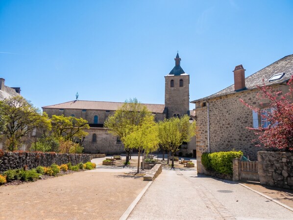 A historic stone building with a tower, a paved courtyard, and benches. - Homerez - Charming House Peyrusse le Roc, Garden (Peyrusse le Roc)