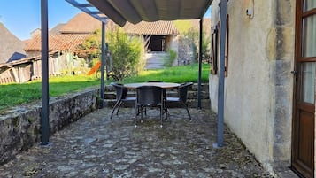Un patio con mesa y sillas, una pérgola y un muro de piedra.