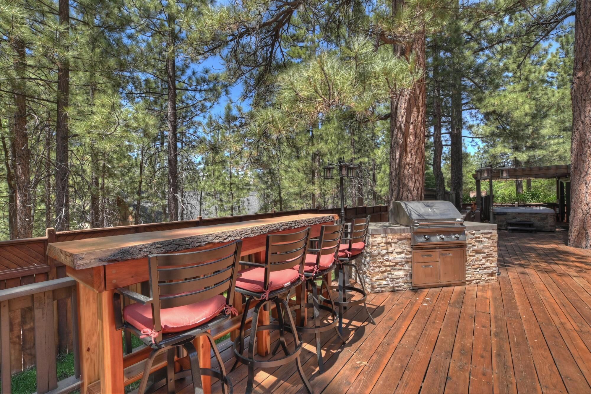Une terrasse extérieure avec une table et des chaises en bois, un barbecue en pierre et une pergola.