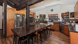 Une cuisine spacieuse avec des meubles en bois, un grand îlot central doté de tabourets et un réfrigérateur en acier inoxydable.