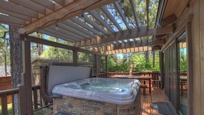 Een hottub onder een houten pergola met stenen muren, omgeven door een terras met banken en een overdekt patio.