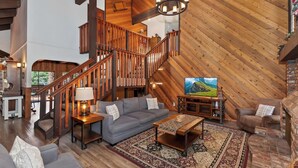 Een ruime loft met een hoge plafond, een houten trap, een grote televisie en een gezellige zithoek met een vloerkleed met dessin.
