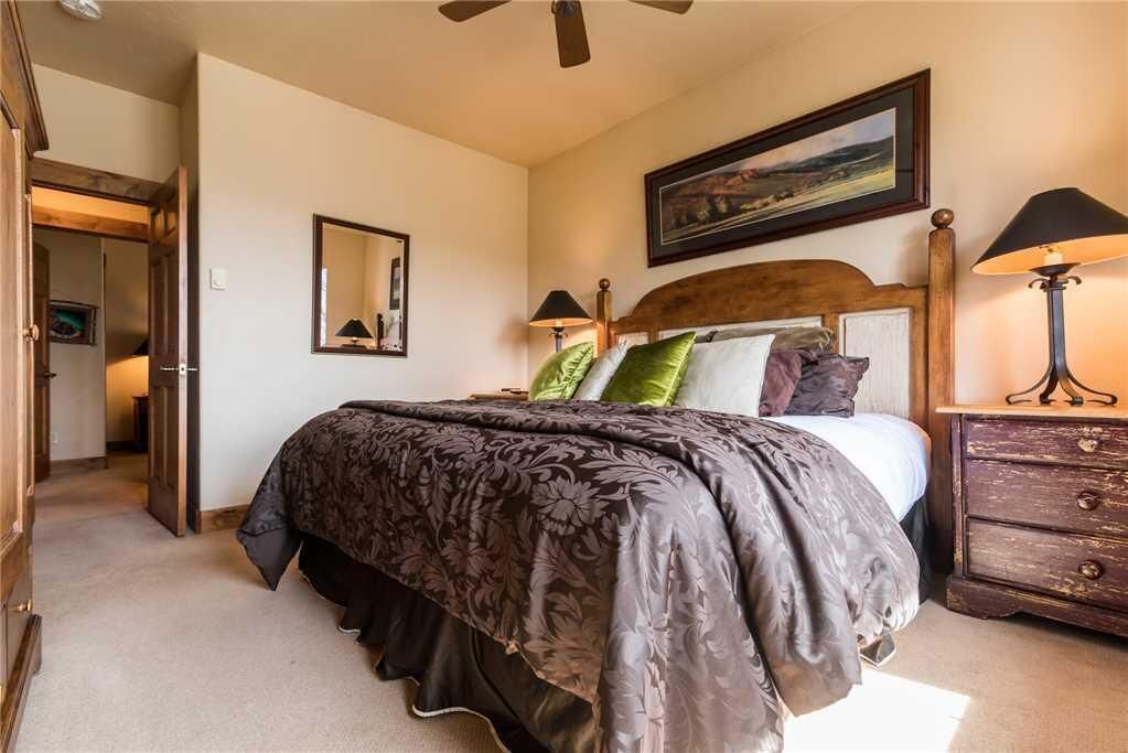 A bedroom with a bed, a nightstand, a lamp, a mirror, and a door leading to another room.
