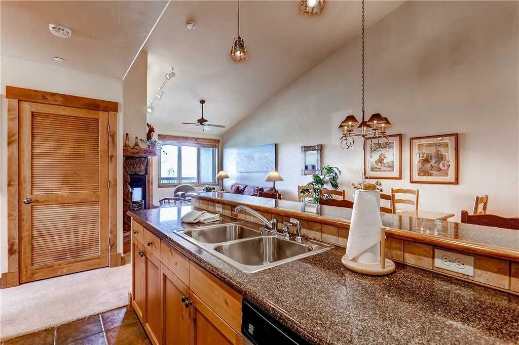 A kitchen with granite countertops, stainless steel sinks, wooden cabinets, and pendant lighting.