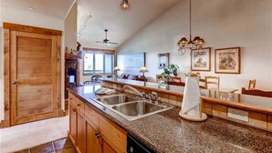 Cocina con encimeras de granito, lavamanos de acero inoxidable, armarios de madera e iluminación colgante.