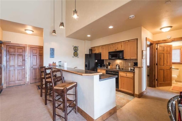 A kitchen with wooden cabinets, a central island with bar stools, a refrigerator, microwave, and a dishwasher.