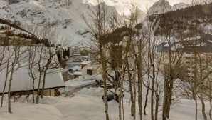 A snow-covered village with buildings and bare trees in the foreground, and mountains in the background.