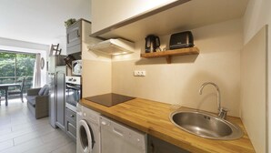 A compact kitchen with a washing machine, a built-in oven, and a coffee maker on a shelf.