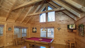 A wooden cabin with a pool table, a clock, and a television.