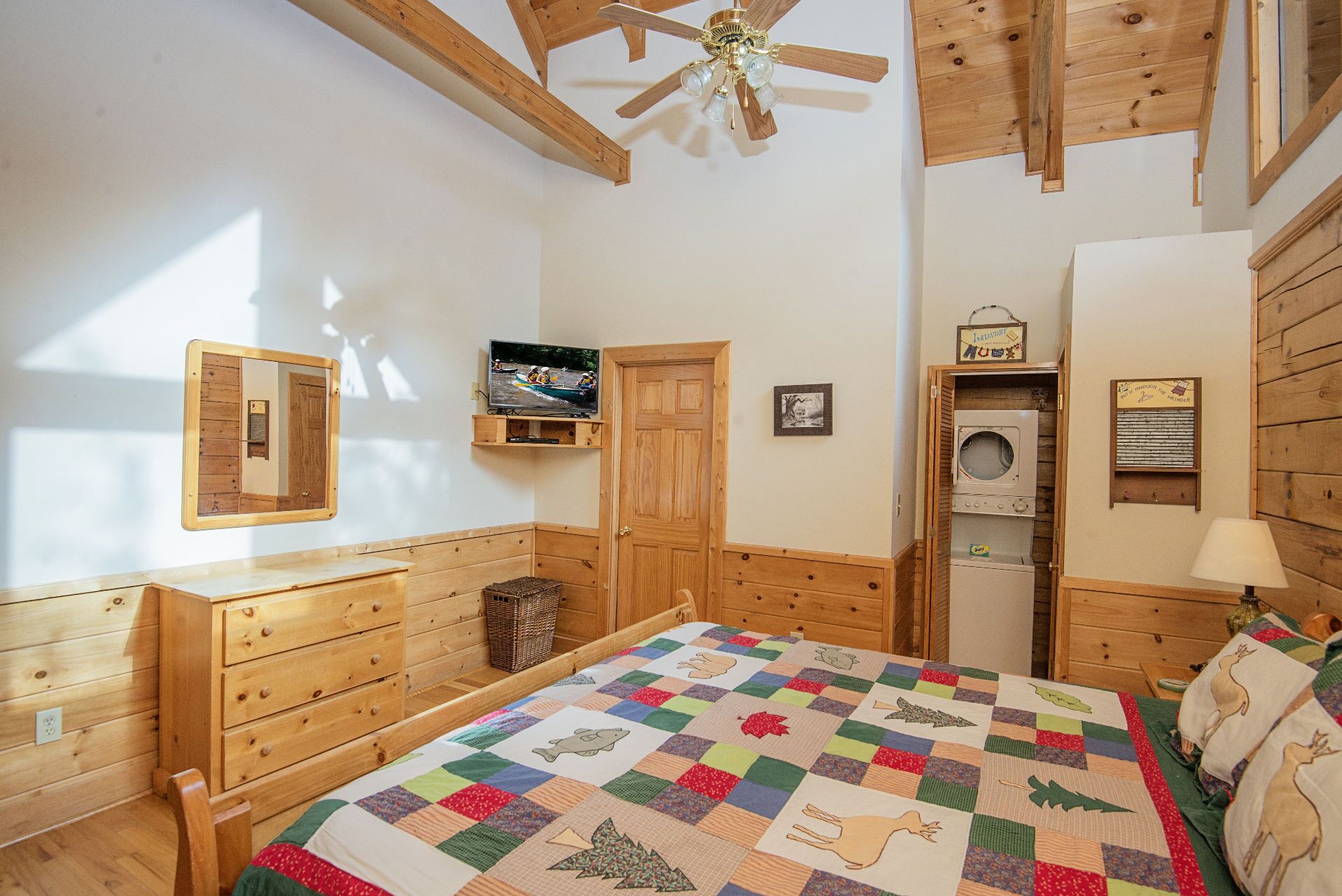 Een gezellige kamer met een houten bed, een televisie, een wasmachine en een plafondventilator.