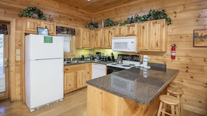 A wooden cabin-style kitchen with a refrigerator, microwave, stove, and bar stools.