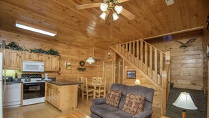 A wooden cabin interior with a kitchen, dining area, and living room.