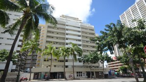 A multi-story hotel with a flat facade, palm trees, and a clear blue sky.