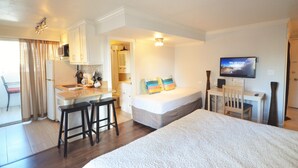 A compact hotel room with a kitchenette, a bed, a desk, and a TV.