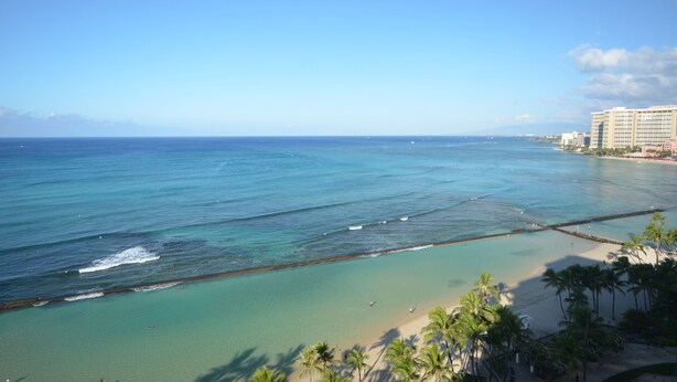 A coastal view with a clear beach, ocean, and a hotel in the background.