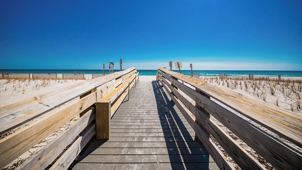 Un muelle de madera que lleva a una playa con cielos despejados.