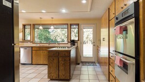 Une cuisine moderne avec des meubles en bois, un réfrigérateur en acier inoxydable, un four et une fenêtre donnant sur un espace verdoyant.
