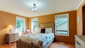 Une chambre à coucher avec un lit en bois, une table de chevet avec une lampe et deux fenêtres équipées de stores.