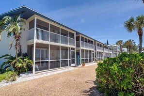 A two-story motel with balconies, a gravel driveway, and tropical landscaping.