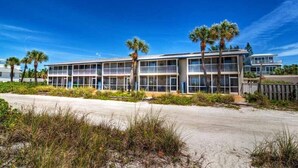 Un hotel frente a la playa con varios balcones, palmeras y una playa de arena.