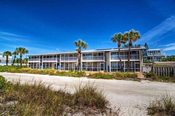 A beachfront hotel with multiple balconies, palm trees, and a sandy beach.